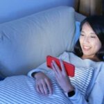 Woman watching movie on phone while laying on couch smiling